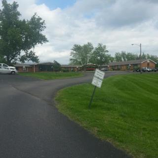 A view of a curved road bordered by grass and trees, featuring a sign that appears to be leaning.