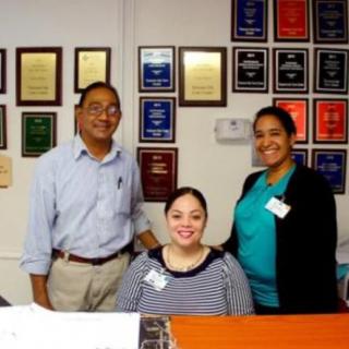 A group of three people smiling in an office with award plaques on the wall.