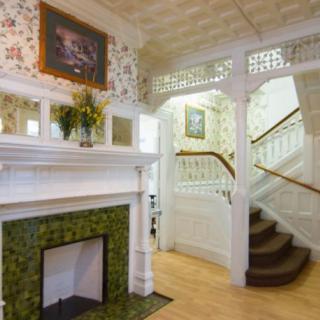 A cozy, vintage interior featuring a fireplace with tile details and a classic staircase adorned with wallpaper and wood accents.