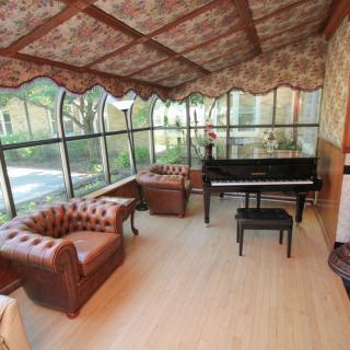 A cozy room featuring a grand piano and leather armchairs, surrounded by large glass windows.