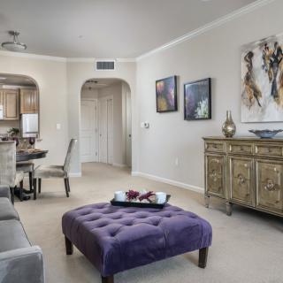 A stylish living room with a purple ottoman and elegant decor leading into a dining area.