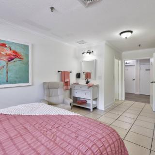 A modern bedroom with a tiled floor, featuring a bed with a pink comforter and wall artwork.