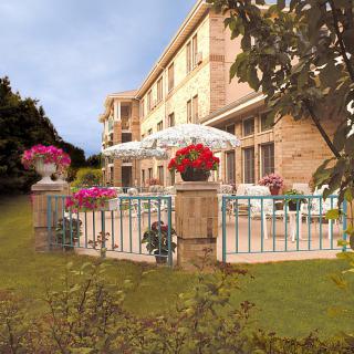 A charming apartment building with a fenced patio adorned with colorful flowers and umbrellas.