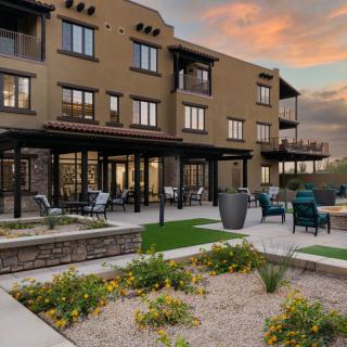A modern apartment building with outdoor seating and landscaped gardens at sunset.