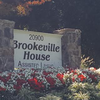 The entrance sign for Brookeville House, an assisted living facility, surrounded by vibrant flowers.