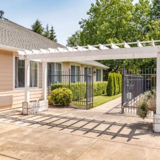 A residential home with a white pergola over the driveway, surrounded by a well-maintained garden.