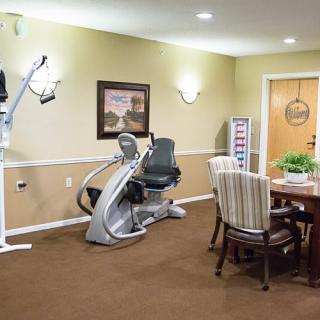 A well-lit fitness room featuring a recumbent exercise bike and a seating area with a table and chairs.