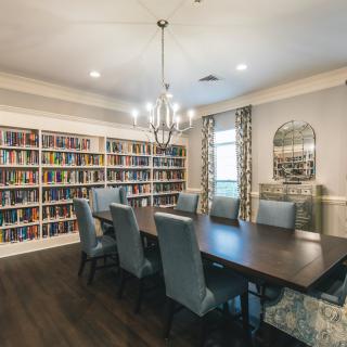 A cozy library and dining room with bookshelves lining the walls and a large table beneath a chandelier.
