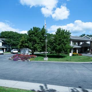 A quiet suburban street lined with trees and residential houses under a partly cloudy sky.