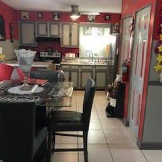 A modern kitchen with red walls and grey cabinets, featuring a dining area with a table and chairs.
