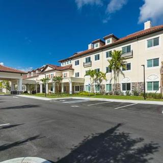 A sunny day view of a residential building with palm trees and a parking lot.