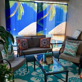 A cozy patio seating area with tropical-themed decor, featuring colorful cushions and a glass table.