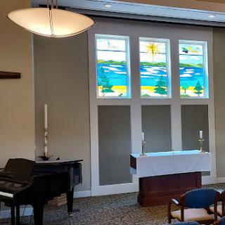 A serene chapel interior featuring stained glass windows and a piano.