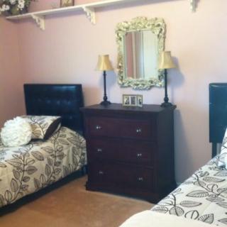 A cozy bedroom with twin beds, a dresser with lamps, and a decorative mirror.