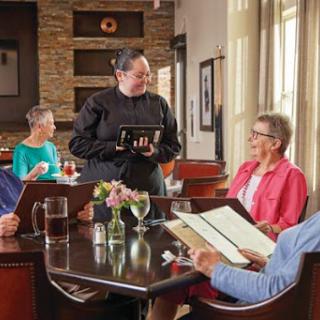 A group of diners are engaged in conversation with a waiter at a restaurant.