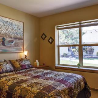 A cozy bedroom featuring a large bed, artwork on the wall, and a window with natural light.