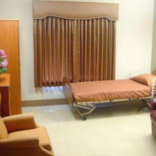 A clean and organized hospital room with a single bed, an armchair, and a window with brown curtains.