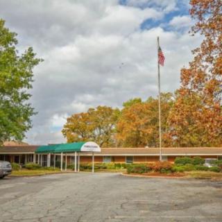 A building with a flagpole in front, surrounded by autumn trees under a cloudy sky.