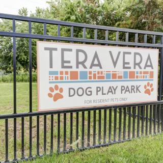 A sign for Tera Vera Dog Play Park displayed on a metal fence in an outdoor setting.