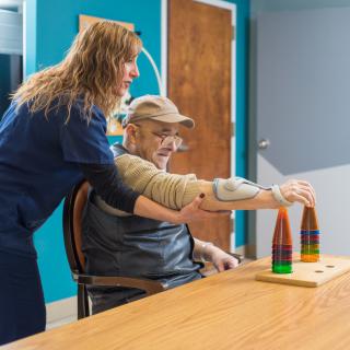 A caregiver assists an elderly person during a physical therapy session.