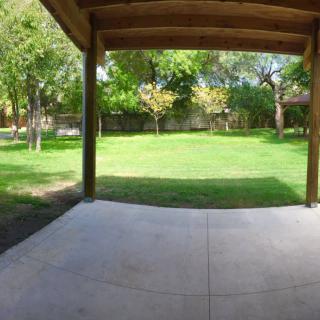 A view from a covered patio overlooking a lush green backyard with trees.