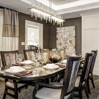 An elegantly designed dining room featuring a large table set with fine dinnerware, surrounded by classic chairs and illuminated by a modern chandelier.