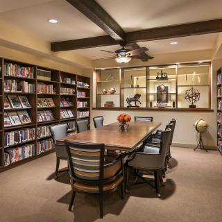 A cozy library room with a central table surrounded by chairs and bookshelves.