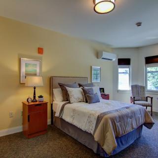 A cozy bedroom with a neatly made bed, bedside lamp, and windows letting in natural light.