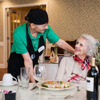 A waiter interacting warmly with an elderly woman at a restaurant table.