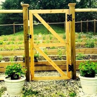 A wooden garden gate with planters on each side, leading to a lush garden.