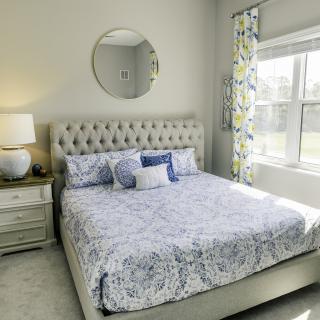 A cozy bedroom featuring a tufted bed with patterned bedding, a round mirror above the headboard, and a lamp on the bedside table.
