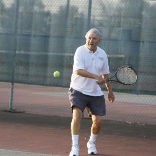 A senior man playing tennis on an outdoor court.