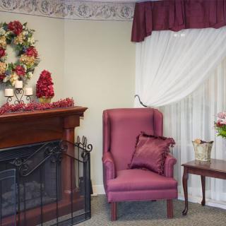 A cozy living room corner featuring a maroon armchair, fireplace with floral decorations, and elegant curtains.