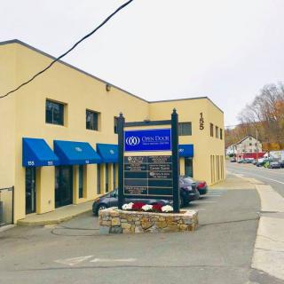 A commercial building with blue awnings and a business sign in the parking lot on an overcast day.
