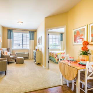 A cozy apartment living area with comfortable seating, a dining table, and large windows allowing natural light.