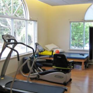 A well-lit gym with exercise equipment including a treadmill and a recumbent bike.