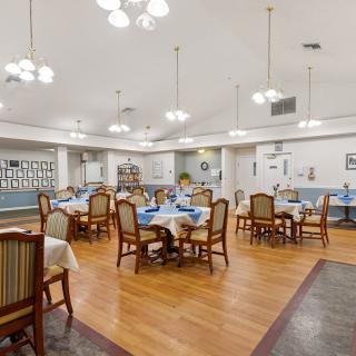 A spacious dining room with neatly arranged tables and chairs, bright lighting, and a polished wooden floor.