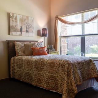 A cozy bedroom with a single bed near a window, decorated with warm tones and artwork.