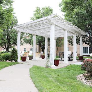 A serene outdoor space featuring a white pergola surrounded by lush greenery and a winding pathway.