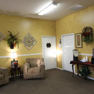 A cozy waiting room with yellow walls, adorned with artwork and plants, featuring comfortable seating.