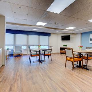A spacious and well-lit dining area within a care facility, featuring tables and chairs arranged for social gatherings.
