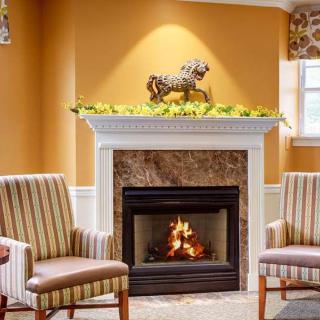 A cozy living room with a fireplace, flanked by two striped chairs and adorned with a decorative horse figure above the mantel.