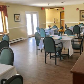 A well-lit dining room with neatly arranged tables and chairs, featuring elegant decor and large windows.