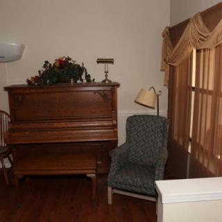 A cozy corner featuring an upright piano and a comfortable chair with a floor lamp beside it, adorned with decorative curtains.