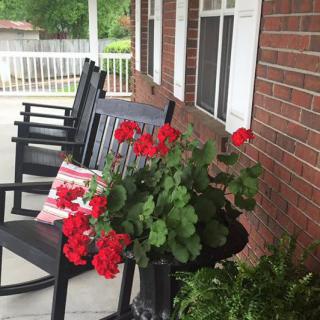 A cozy porch with black rocking chairs and vibrant red geraniums in a pot.