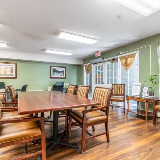 A well-lit conference room with a large wooden meeting table and chairs, featuring green walls and artwork.