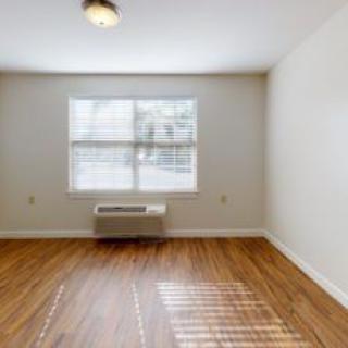 A bright, empty room with hardwood flooring and a window allowing natural light.