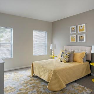 A modern bedroom featuring a neutral gray and yellow color scheme, with natural light streaming through the windows.