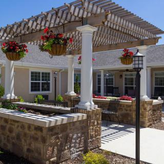 A charming patio area with a pergola and hanging plants, featuring a stone wall and a lamp post.