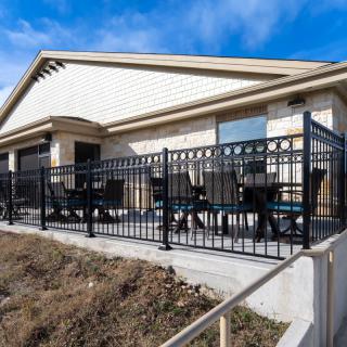 A single-story building with an outdoor patio area featuring black railings and seating, set against a clear blue sky.